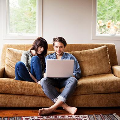 a couple sitting on a couch looking at a laptop
